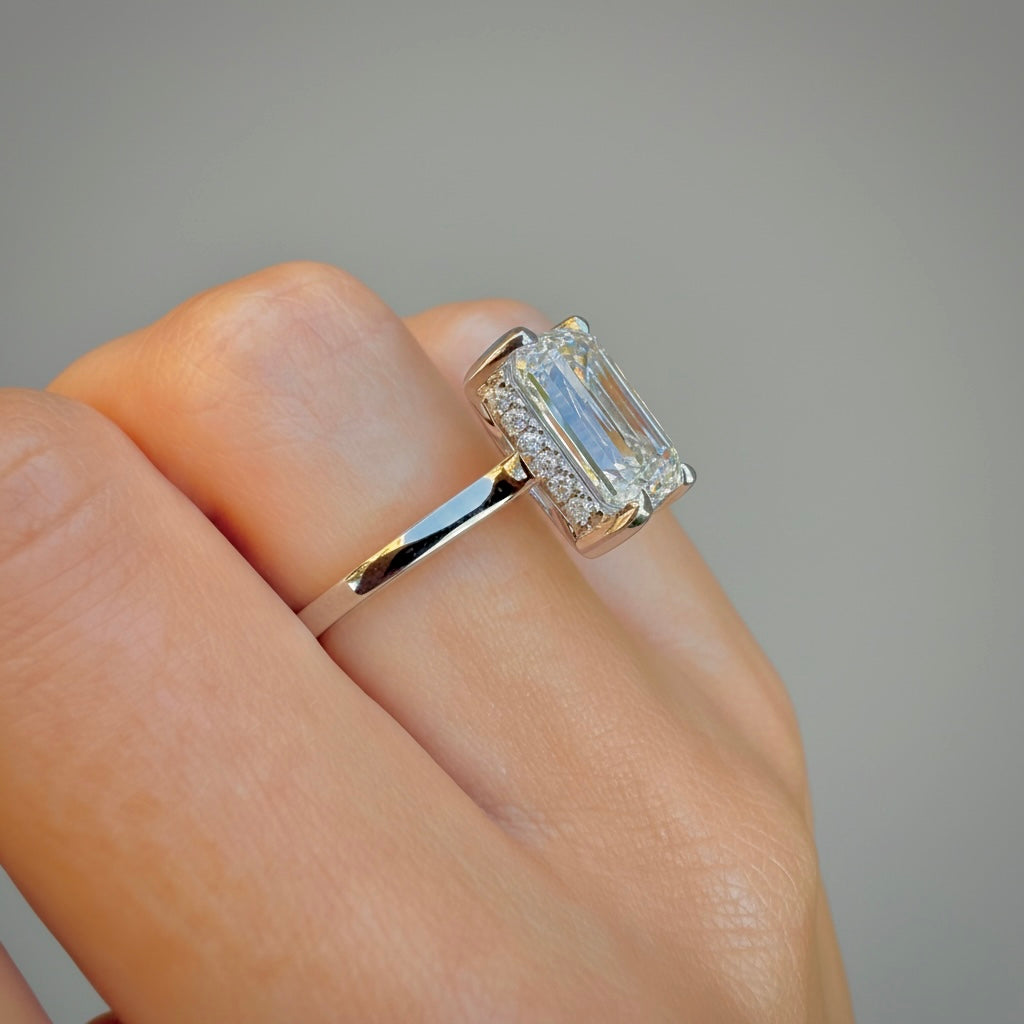 Hidden halo of round accent diamonds around the emerald-cut center stone, close-up detail