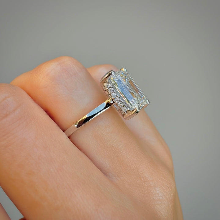 Hidden halo of round accent diamonds around the emerald-cut center stone, close-up detail